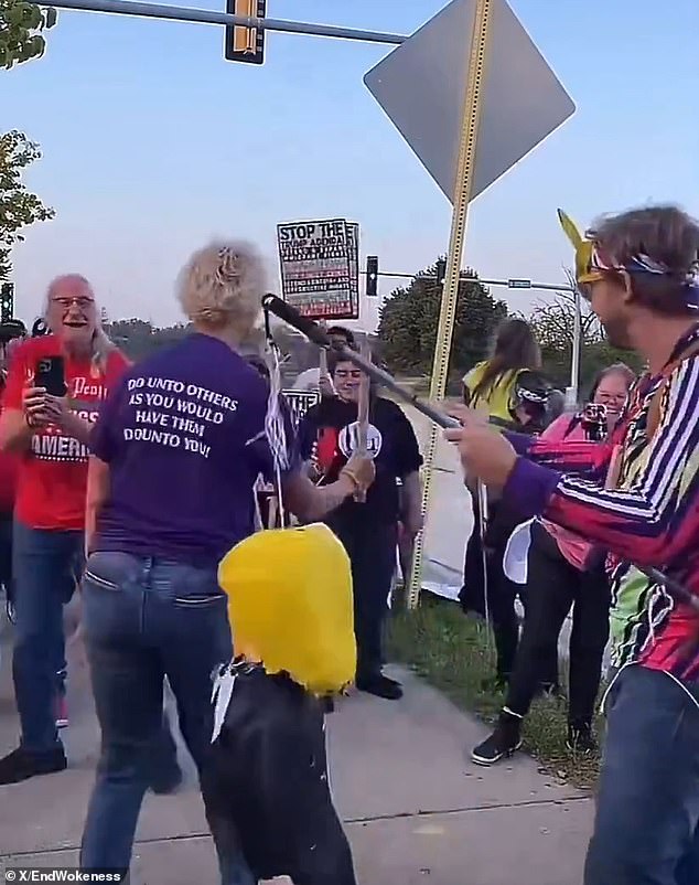 Protester wearing kindness shirt smashes piñata of Trump with pipe.