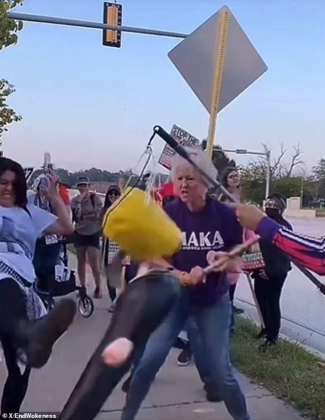 Protester wearing kindness shirt smashes piñata of Trump with pipe.